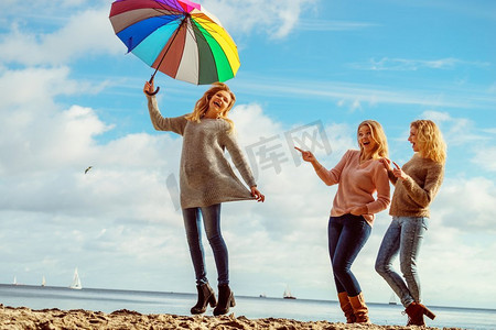 三个女人充满欢乐，一起度过美好的时光。一个女人拿着五颜六色的雨伞。妇女拿着伞与朋友的乐趣