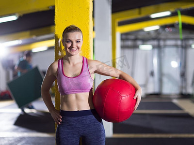 美丽的运动员妇女的肖像与红色的医疗球在crossfit健身房。肖像的女人与红色交叉健身球
