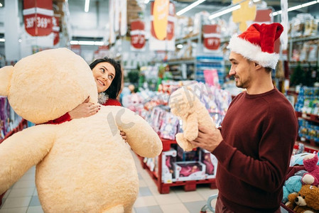 年轻夫妇选择毛绒玩具圣诞节在超市，家庭传统。12月购买新年节日商品和装饰品