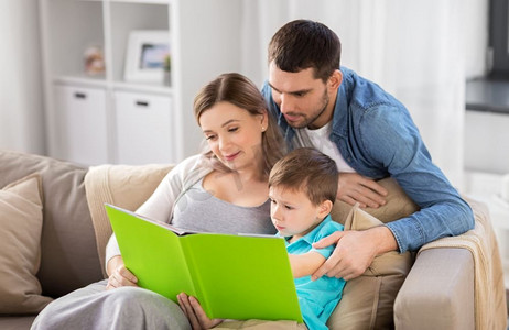 人和家庭概念—快乐的母亲，父亲和小儿子在家里的沙发上看书。快乐的家庭阅读书在家里