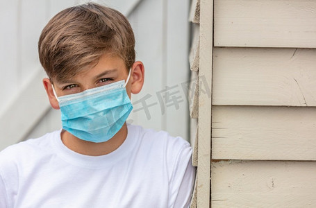 在冠状病毒COVID—19病毒大流行期间，男孩十几岁的男孩戴着面罩在外面靠在房子的一边