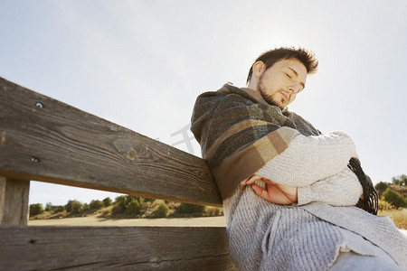 一个坐在头上的年轻人睡觉和享受早晨秋天的阳光与背光从蓝天