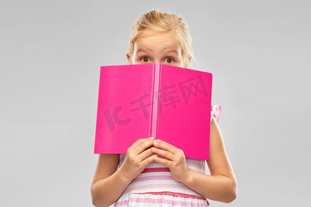 童年和人的概念—隐藏在灰色背景书后面的小女孩。小女孩躲在书上