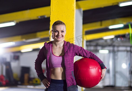 美丽的运动员妇女的肖像与红色的医疗球在crossfit健身房。肖像的女人与红色交叉健身球