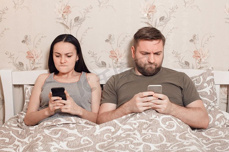 年轻夫妇在一张床上与手机在手。
