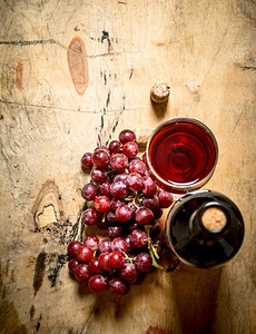 一串红葡萄和一瓶葡萄酒。在木质背景上..一串红葡萄和一瓶葡萄酒。