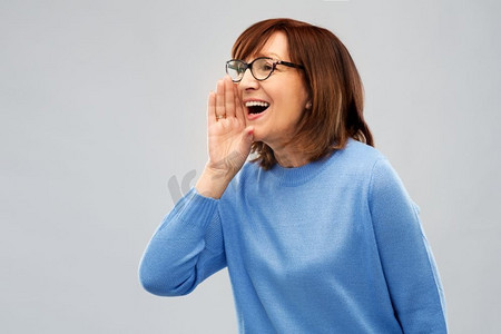 公告和老年人概念—高级妇女在眼镜呼叫在灰色背景。戴眼镜的高级妇女呼叫灰色