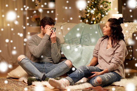 圣诞节，技术和人的概念—愉快的夫妇与相机拍摄在家里超过雪。快乐的夫妇与相机拍摄在家里