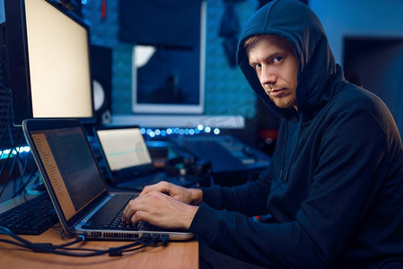戴着兜帽的黑客坐在笔记本电脑前，信息黑客。互联网间谍，试图侵入加密网络的男性程序员
