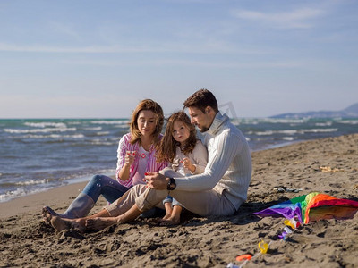 年轻的家庭享受在秋天的一天矢量。家庭与小女儿休息和有乐趣使肥皂泡在海滩在秋天