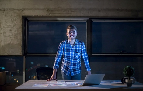年轻男性工程师在建筑工地检查文件和业务工作流程使用膝上型计算机在晚上新的启动办公室