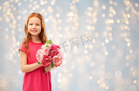 童年和人概念—快乐的红头发女孩有花在节日光背景。快乐的红头发的女孩与花在灯