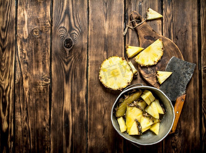 用斧头把菠萝片放进锅里。在一张木桌上。用斧头把菠萝片放进锅里。