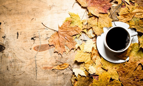秋天加摄影照片_秋天的风格。一杯加枫叶的热咖啡。在木制背景上。秋天的风格。一杯加枫叶的热咖啡。