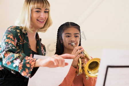 教师在音乐课上帮助女学生吹小号