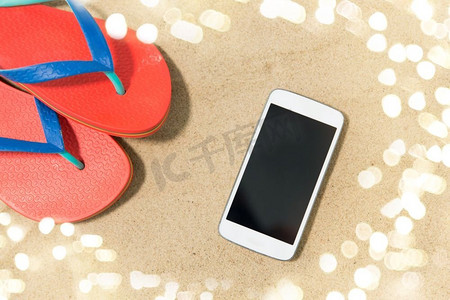 技术，假期和暑假概念—智能手机和人字拖在沙滩上。智能手机和人字拖在沙滩上