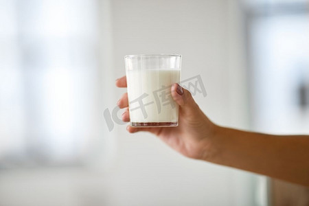 食物，吃和奶制品概念—女性手拿着牛奶的玻璃特写镜头。关闭的女性手拿着杯牛奶