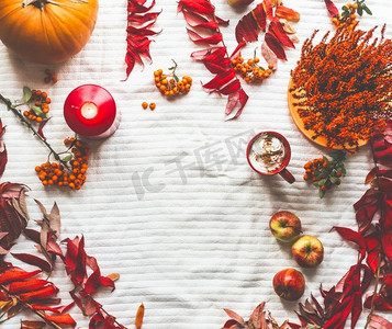 秋天的框架由南瓜，红色的秋叶，卡布奇诺，蜡烛和苹果在白色毯子上制成。俯视图。平铺