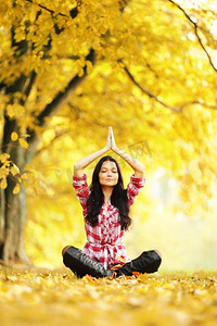 瑜伽美容摄影照片_美丽的年轻女子坐在莲花瑜伽的位置在秋天公园。秋天瑜伽女人