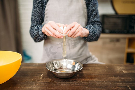 甜饼摄影照片_女性将鸡蛋打碎放在木桌上的碗里。甜饼烹调准备。面团制作