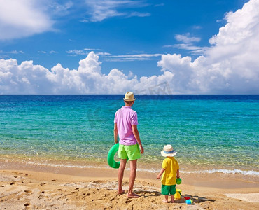 2岁的蹒跚学步的男孩在海滩上与父亲，拿着充气戒指。暑假家庭度假。希腊，西托尼亚。 