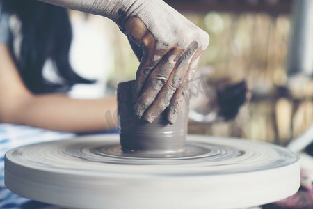 陶瓷工艺摄影照片_女人的双手合拢，精湛的陶瓷工作室用陶工的轮子上的粘土’’