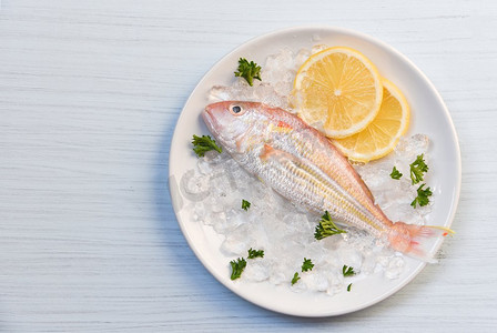 海鲜鱼摄影照片_海鲜鱼板海洋美食新鲜的鱼在冰柠檬欧芹在白色板桌子背景顶视图