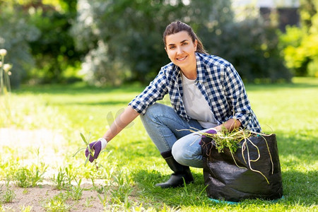 园艺和人的概念-快乐的微笑的女人，在夏季花园的袋子除草花坛。一名妇女在为夏园的花坛除草。