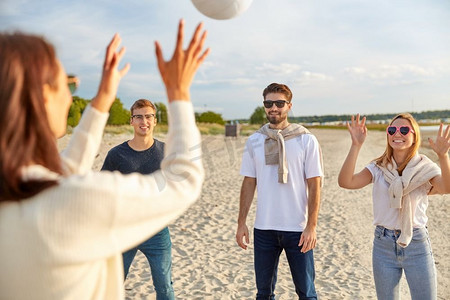 打排球的摄影照片_排球，休闲游戏和人的概念—快乐的朋友在沙滩上玩球在夏天。夏天在沙滩上打排球的朋友