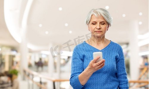 技术，销售和老人概念—高级妇女使用智能手机在购物中心背景使用智能手机的老年妇女