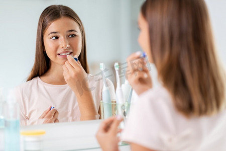 美容和化妆品概念—少女应用唇膏和寻找镜子在家庭浴室。十几岁的女孩应用唇膏在浴室