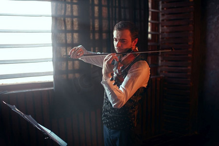 演奏背景摄影照片_男小提琴家在窗户上演奏小提琴。带乐器的小提琴手