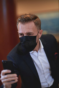 公司商人戴面罩和使用智能电话在豪华办公室