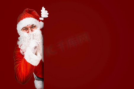 圣诞老人用手指在嘴唇上要求安静与彩色广告板和复制空间。圣诞老人要求安静