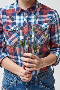 女孩拿着一件漂亮的蓝色花，背景是格子衬衫。母亲节。手持蓝花杏花的女孩