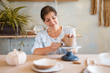 一个小学生卡通摄影照片_女陶工皮壶、制陶车间。女人塑造一个碗。手工陶艺，用粘土制作的餐具