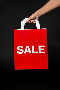 销售，消费主义和出口概念手拿红色购物袋在黑色背景手拿红色购物袋，上面写有销售字样