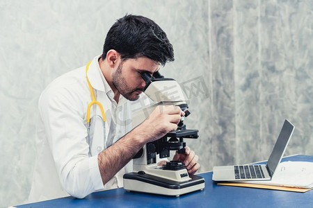 在医院实验室使用显微镜的年轻男医生。医药科技研发理念。