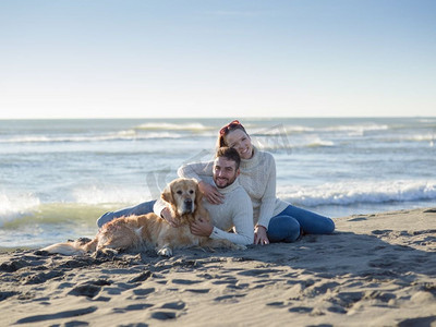 秋日时光摄影照片_情侣和一只狗一起在秋日的海滩上享受时光。与狗在海滩上享受时光的情侣