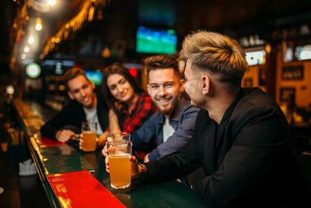 喝啤酒摄影照片_快乐的球迷在体育酒吧的柜台前喝啤酒，庆祝胜利。快乐的足球迷举起酒杯喝啤酒