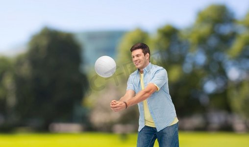 体育，休闲和人概念—微笑的年轻人打排球在夏天公园背景。微笑的男子打排球超过夏季标准杆