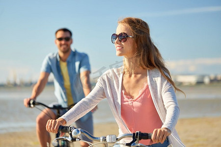 骑情侣摄影照片_人，休闲，生活理念-快乐的年轻夫妇在海滩上骑自行车。幸福的年轻夫妇在海边骑自行车