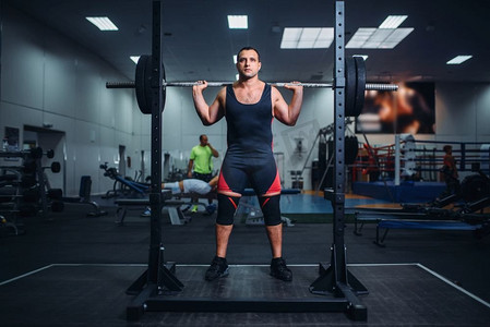 健身房里，一名肌肉发达的运动员准备用杠铃做深蹲。举重训练、力量举重训练