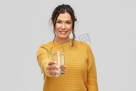 液体穿透摄影照片_人物概念-快乐微笑的年轻女子的肖像，在灰色背景下，玻璃杯里的水。微笑的年轻女子端着玻璃杯里的水