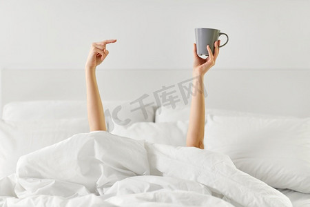 早晨，舒适和人的概念-年轻的女人，一杯咖啡躺在家里卧室的床上。躺在床上端着一杯咖啡的女人