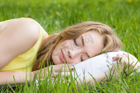 年轻女子睡在新鲜的春天草白色枕头。女人睡在草地上