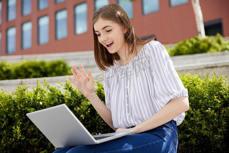 年轻女大学生或办公室工作人员与笔记本电脑有视频聊天户外在大学校园