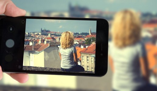 情感博主摄影照片_在布拉格，一名博主拍摄了一名坐在屋顶上的智能手机。坐在房顶上的女孩