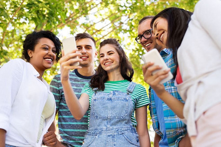友谊，技术和国际概念—一群朋友与智能手机在夏季公园。快乐的朋友与智能手机在夏季公园