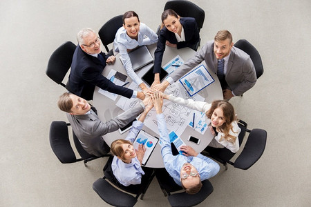 合作的双手摄影照片_企业、人员和团队合作的概念—快乐的业务团队坐在桌子堆手。快乐的生意人堆积双手